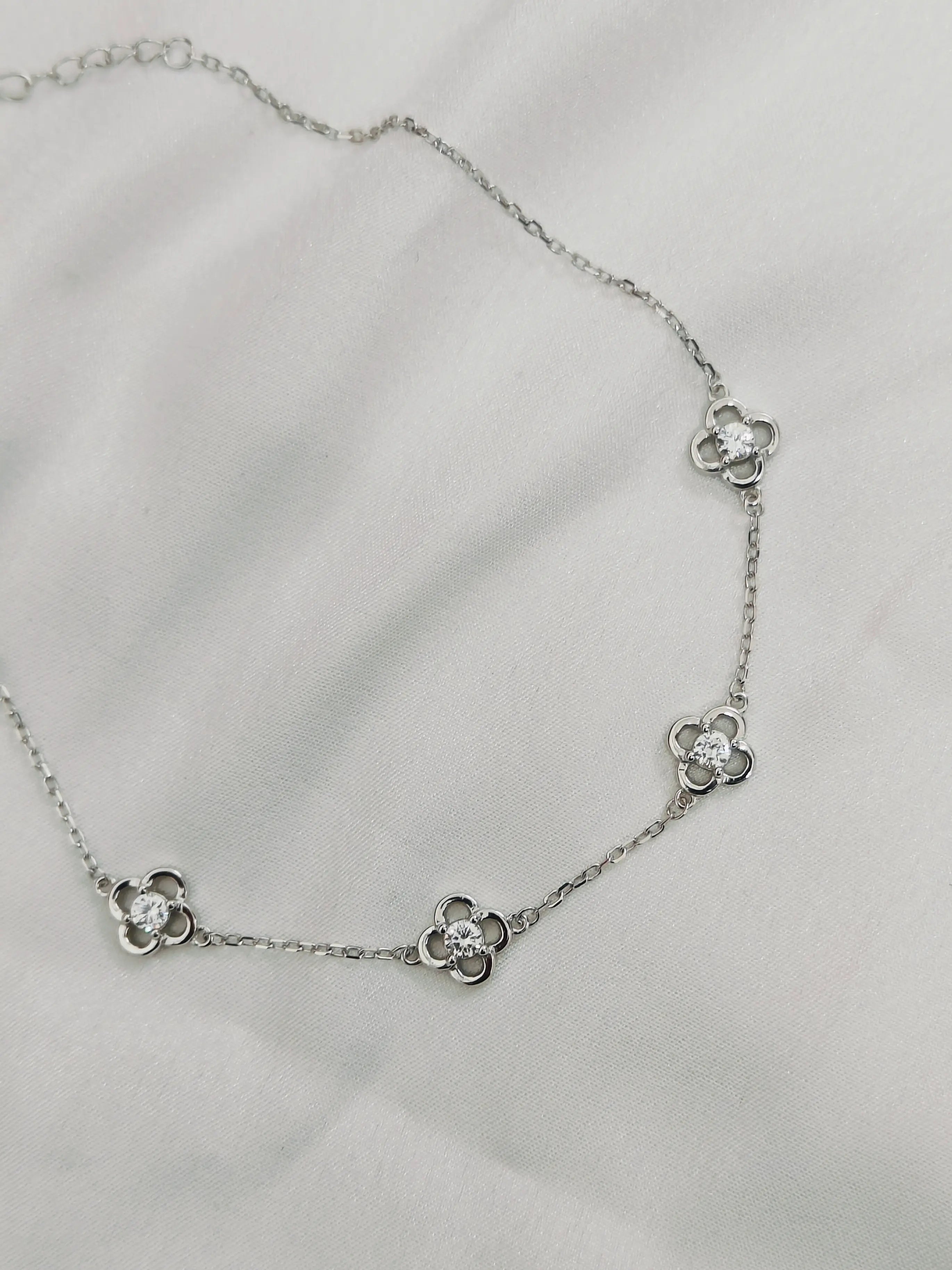Silver necklace with flower-shaped pendants on a light gray background